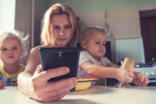 moeder op telefoon met twee jonge kinderen op schoot